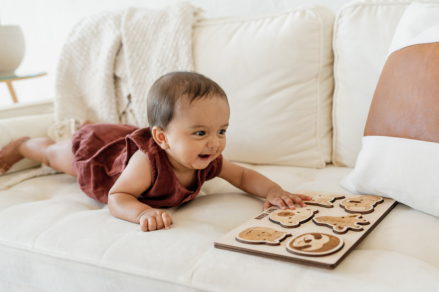 A thrilled baby playing with a custom laser-cut wooden puzzle with laser-engraved animal faces.